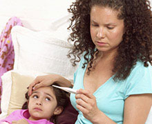 Mom reading thermometer with hand on child's forehead 