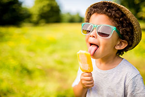 A boy in sunglasses licks a popsicle in a field