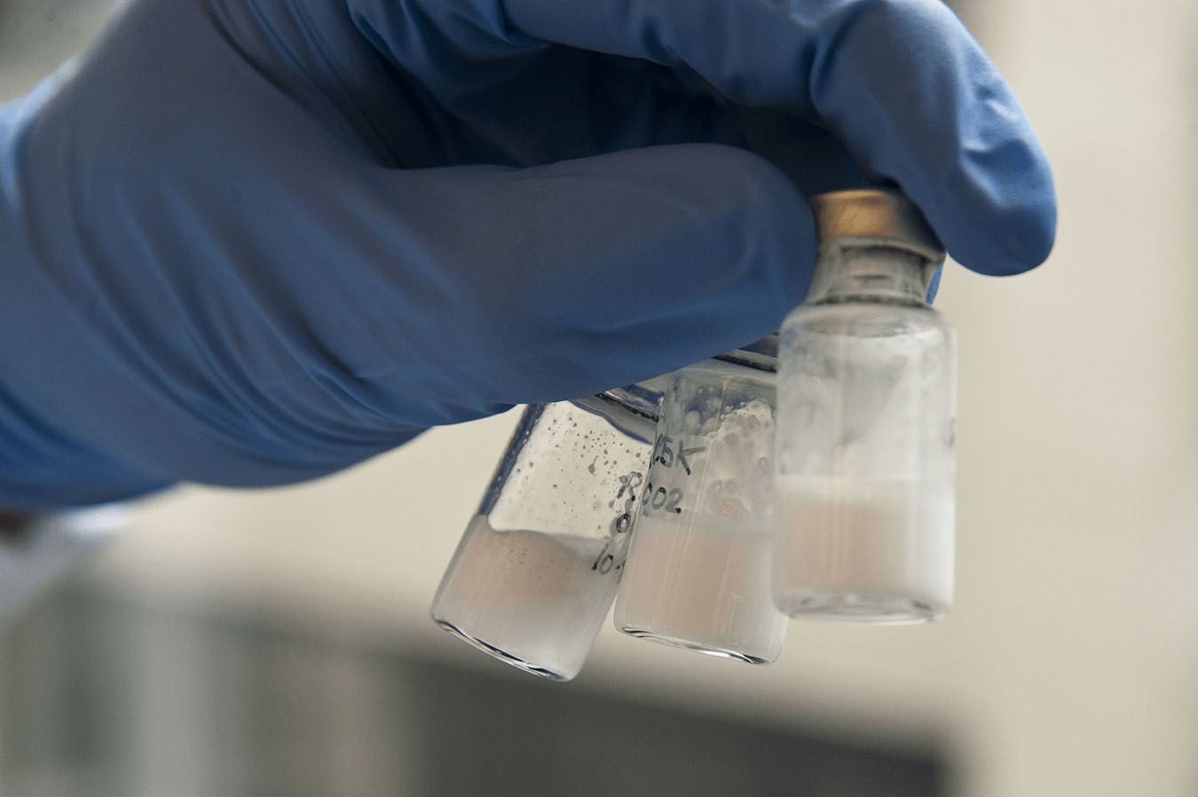 A gloved hand holds three vials of milky-white substance